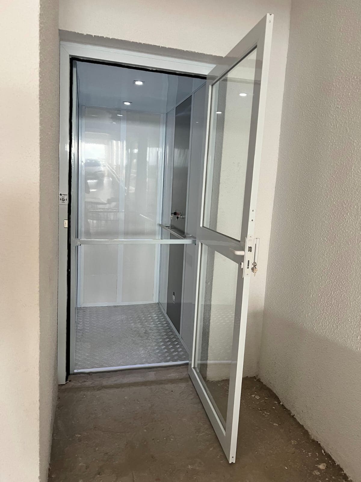 Porta de pavimento aberta dando acesso à cabine prateada de plataforma residencial