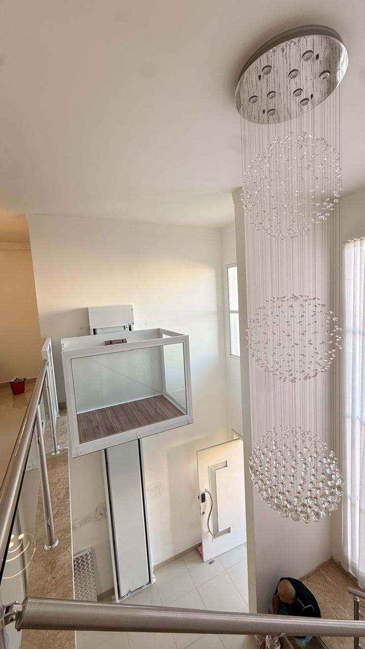 Plataforma residencial cabinada branca instalada em hall com pé direito duplo e lustre