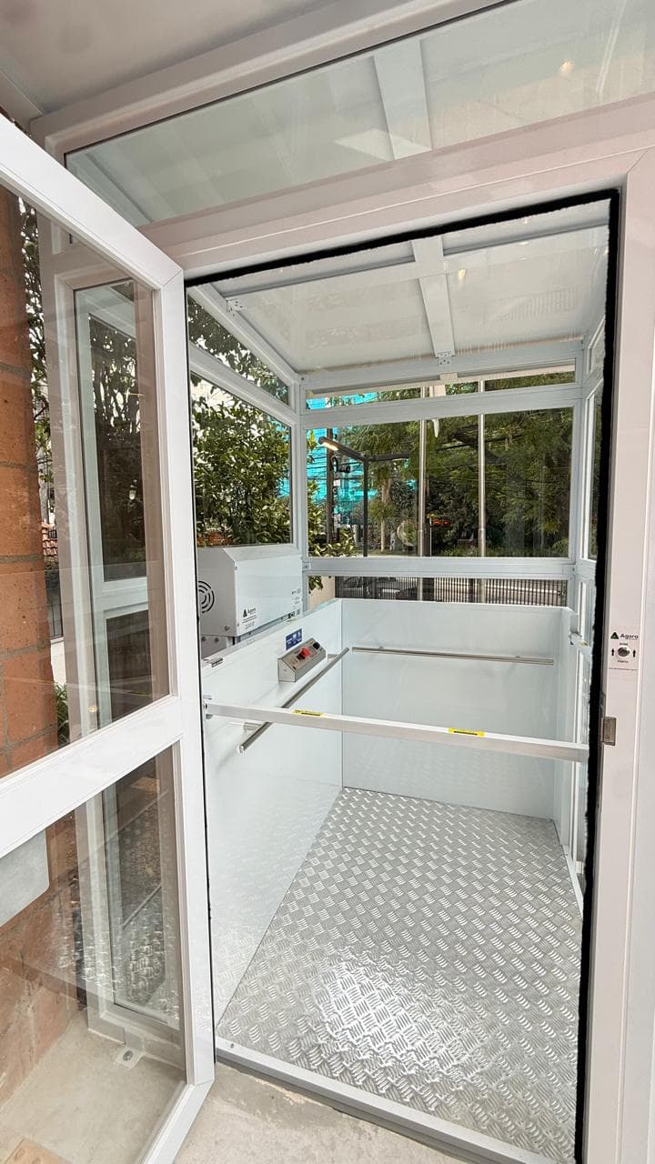 Plataforma residencial cabinada com fechamento panorâmico em vidro instalada em entrada de casa com jardim