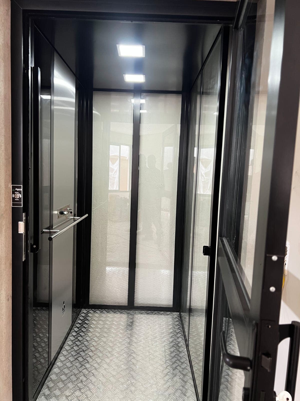 Plataforma residencial cabinada em vidro e estrutura preta instalada em entrada externa